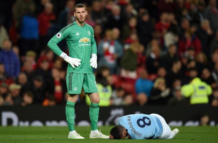 Kiper David de Gea berdiri di samping pemain Manchester City, Ilkay Gundogan yang meringkuk kesakitan. Dalam laga derby Manchester itu, skuat Setan Merah dipermalukan rivalnya dengan skor 2-0, Kamis (25/4/2019). [OLI SCARFF / AFP]