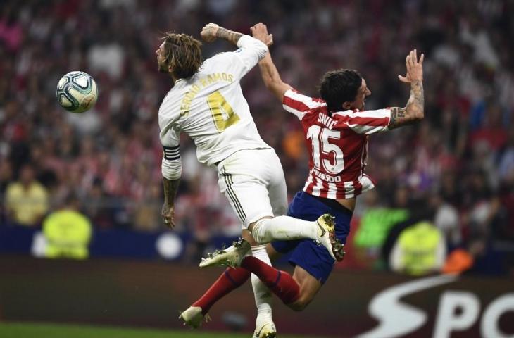 Bek Real Madrid, Sergio Ramos berebut bola dengan bek Atletico Madrid, Stefan Savic. Pada laga derby Madrid yang berlangsung, Minggu (29/9/2019) tersebut laga berakhir imbang tanpa gol. [OSCAR DEL POZO / AFP]