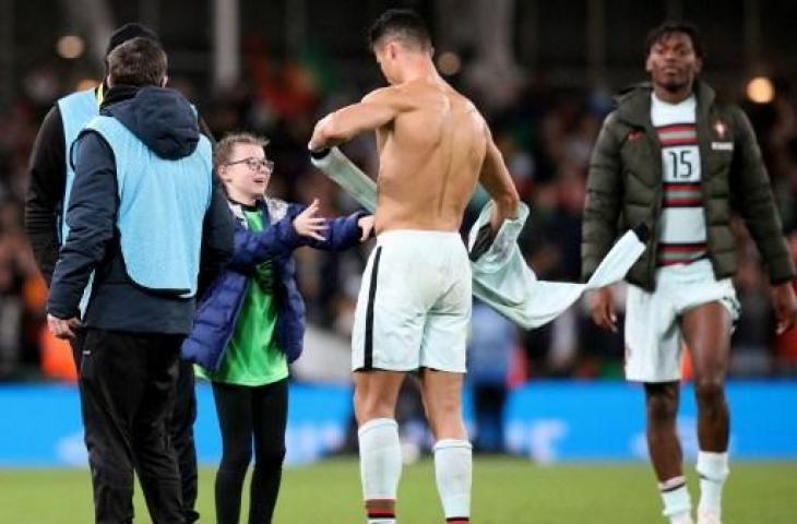 Penyerang timnas Portugal, Cristiano Ronaldo melepas bajunya untuk seorang fan cilik Irlandia yang nekat menerobos masuk lapangan setelah pertandingan lanjutan Grup A Kualifikasi Piala Dunia 2022. (PAUL FAITH / AFP)