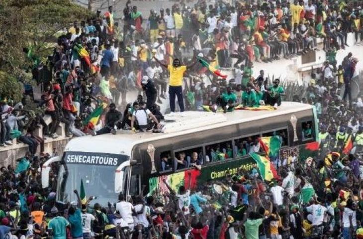 Pendukung bersorak saat pelatih Timnas Senegal, Aliou Cisse mengangkat trofi Piala Afrika 2021 di Dakar pada 7 Februari 2022, setelah memenangkan untuk pertama kalinya. (JOHN WESSELS / AFP)