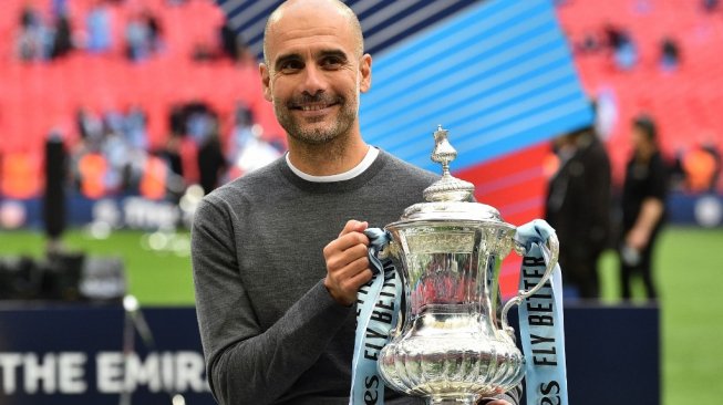 Manajer Manchester City, Pep Guardiola mengangkat trofi Piala FA usai timnya mengalahkan Watford 6-0 pada laga final di Stadion Wembley, London, Minggu (19/5/2019) dini hari WIB. [Glyn KIRK / AFP]