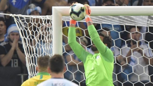 Kiper Timnas Brasil, Alisson Becker menangkap bola yang dilepas Lionel Messi saat tendangan bebas pada semifinal Copa America 2019 di Stadion Mineirao, Belo Horizonte, Brasil, Rabu (3/7/2019) pagi ( Pedro UGARTE / AFP)