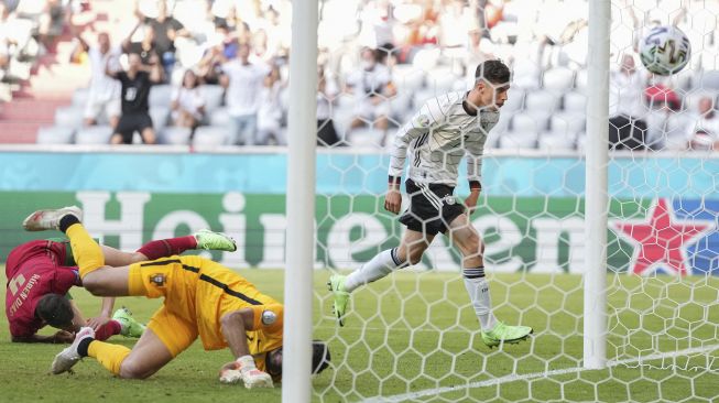 Bek Portugal Ruben Dias (kiri) berguling-guling di tanah setelah membelokkan bola untuk mencetak gol bunuh diri untuk gol pertama Portugal saat pemain depan Jerman Kai Havertz (kanan) merayakan gol selama pertandingan sepak bola Grup F UEFA EURO 2020 antara Portugal dan Jerman di Allianz Arena, Munich pada (19/6/2021). [Matthias Hangst / POOL / AFP]