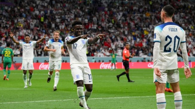 Penyerang Timnas Inggris #17 Bukayo Saka (Tengah) melakukan selebrasi dengan penyerang Inggris #20 Phil Foden setelah mencetak gol ketiga timnya selama pertandingan babak 16 besar Piala Dunia 2022 Qatar antara Inggris vs Senegal di Stadion Al-Bayt di Al Khor, utara Doha pada 4 Desember 2022 waktu setempat atau Senin (5/12/2022) WIB.Paul ELLIS / AFP